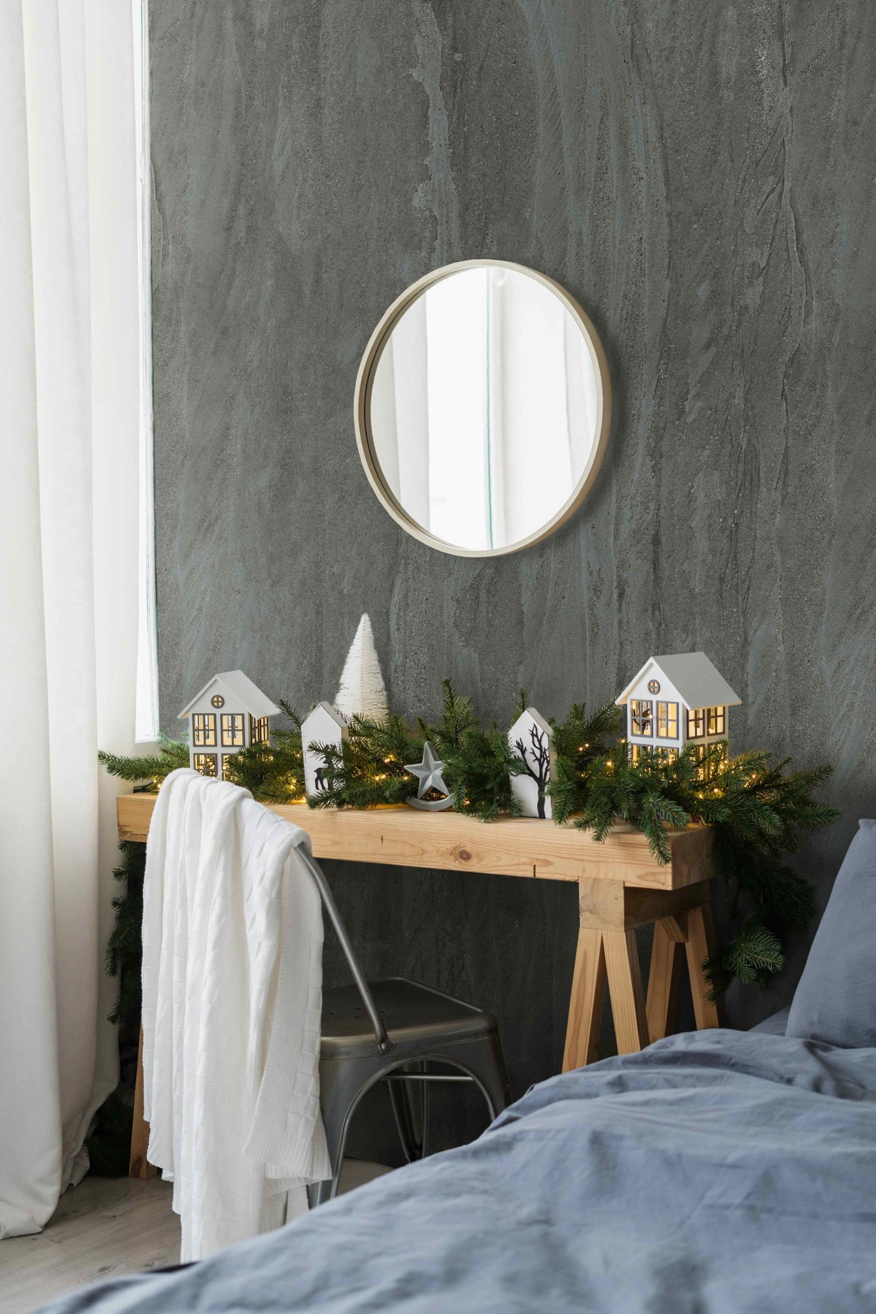 Vertical side view photo of cozy bedroom with loft style interior design, wooden table near bed and green, winter decor on fir garland